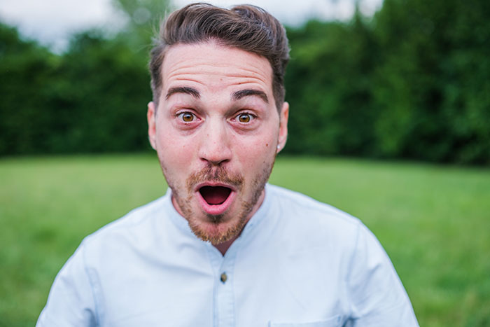 Man wearing light blue shirt outdoors with shocked expression, illustrating rage-baits that can ruin a man’s day.