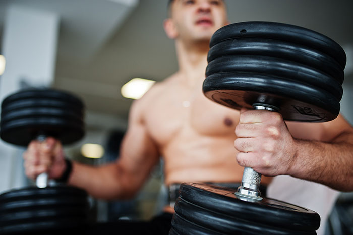 Muscular man lifting heavy dumbbells in a gym, demonstrating strength while exercising with rage-baits intensity.