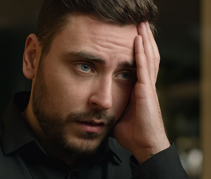 Man looking stressed and frustrated, holding his head, illustrating rage-baits impact on emotions.