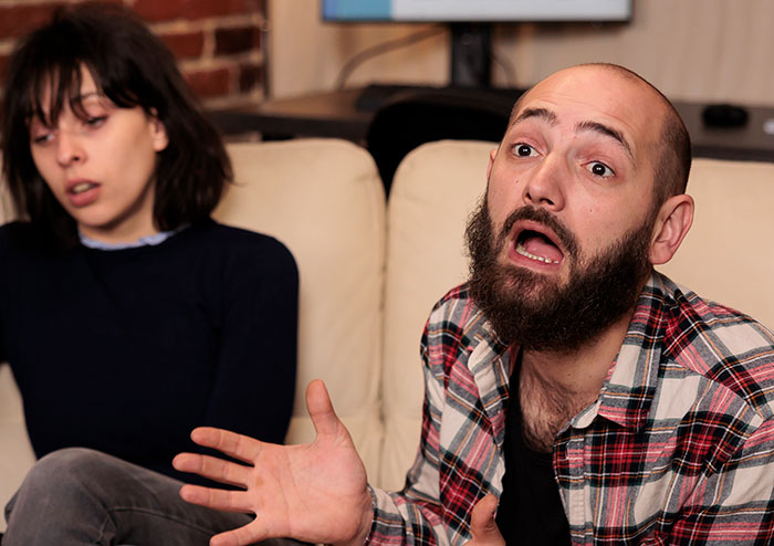 Man reacting with frustration while woman looks away upset during a tense moment showing rage-baits interaction.