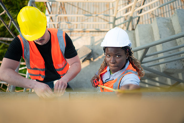 Two construction workers wearing helmets and safety vests measuring a wall, illustrating rage-baits from women.