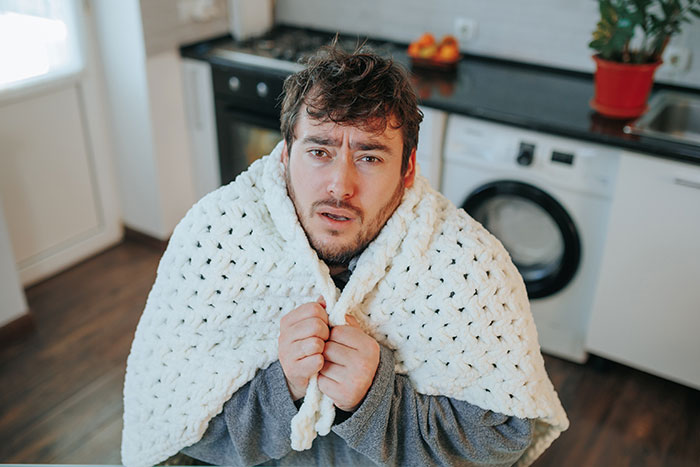 Man wrapped in a white blanket looking upset, illustrating rage-baits from women to ruin a man’s day concepts.