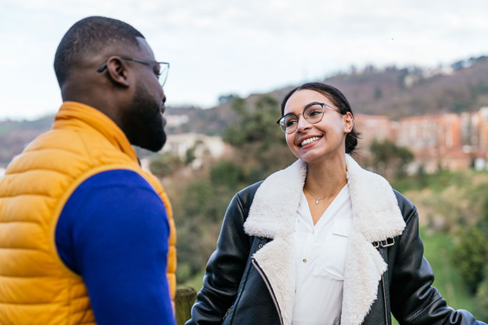 A woman smiling and talking to a man outdoors, illustrating rage-baits and phrases that impact a man’s day.