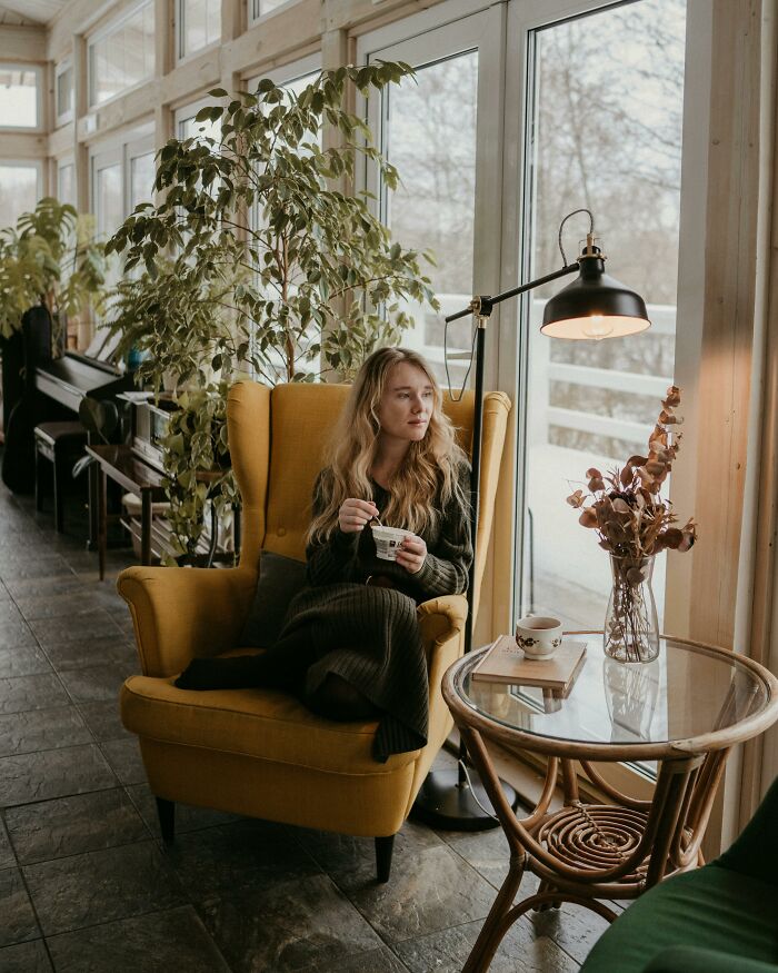 Woman sitting in a yellow chair by the window, looking thoughtful and holding a cup, illustrating grumpy and annoyed feelings.