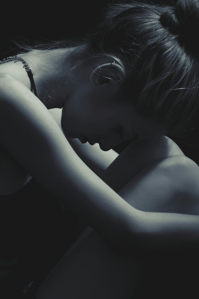 Woman sitting with head resting on knees, expressing feelings of being grumpy and annoyed in a dimly lit setting.