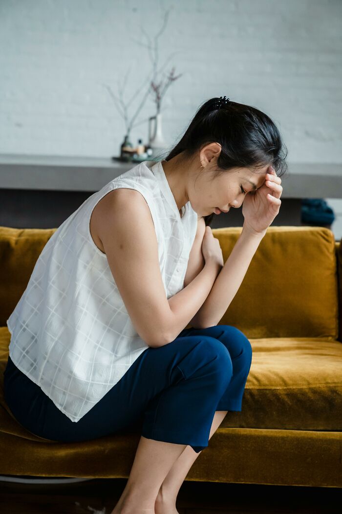 Woman sitting on a sofa looking grumpy and annoyed, reflecting on emotional cases of mankeeping shared by women.
