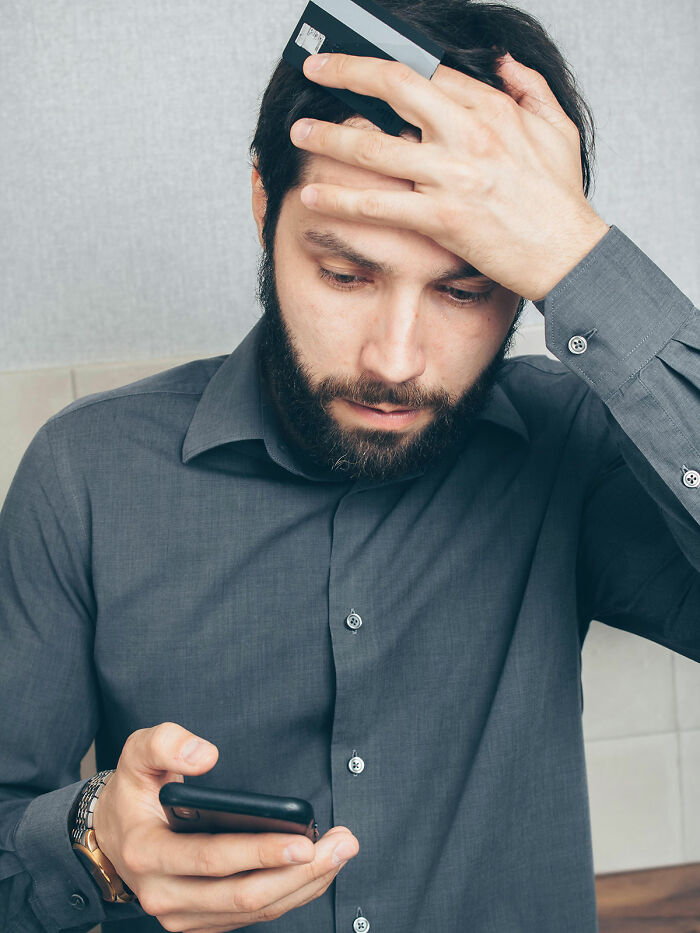 Man looking grumpy and annoyed while holding a phone and credit card, illustrating common cases of mankeeping issues.