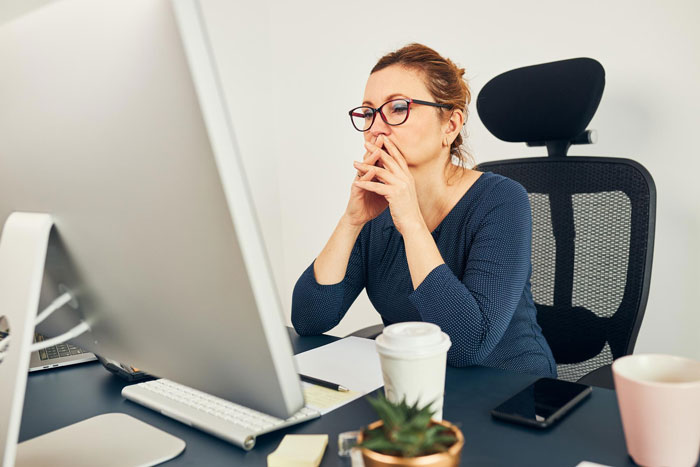 Woman sitting at desk looking concerned while working on computer, depicting employee sidelined and corporate spying on staff.
