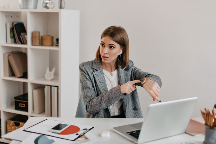 Woman in office checking watch anxiously, illustrating boss blocking Tenerife vacay due to focus concerns with work distractions.