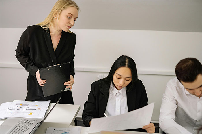 Office Karen leaning over colleagues’ desks, unable to mind her own business while coworkers observe quietly. Office Karen leaning over colleagues’ desks, unable to mind her own business while coworkers observe quietly.