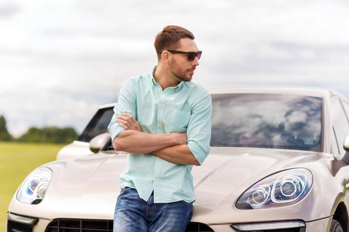 Man leaning on luxury vehicle outdoors, wearing sunglasses and casual shirt, highlighting hubby prioritizing luxury vehicle issue.