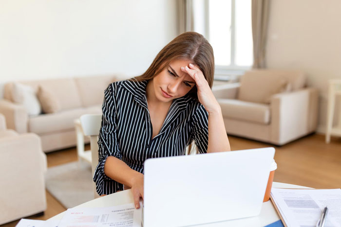 Woman stressed while working on laptop at home, reflecting tension over luxury vehicle and family plans conflict.