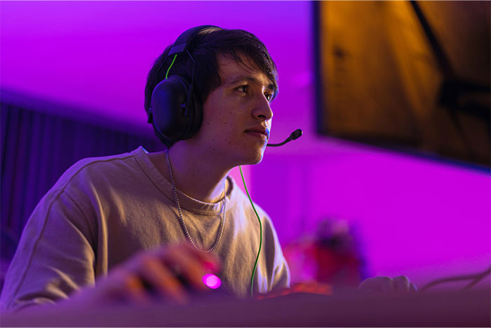 Young man wearing headphones and focused on a computer screen, illustrating ways people got banned from a friend's house.