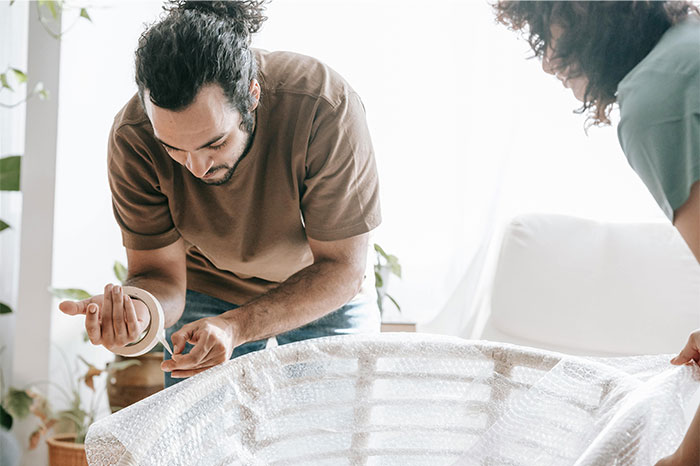 Two friends preparing bubble wrap together in a bright room, illustrating ways people got banned from a friend’s house.