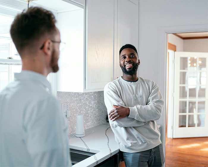 Two men talking in a bright kitchen, illustrating common reasons people got permanently banned from a friend’s house.