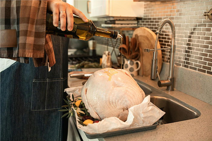 Person in an apron pouring oil on a raw turkey in a kitchen, illustrating ways people got banned from a friend’s house.