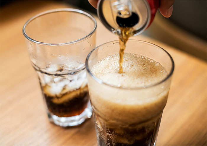 Pouring soda into a glass with ice on a wooden table, illustrating ways people got permanently banned from a friend’s house.