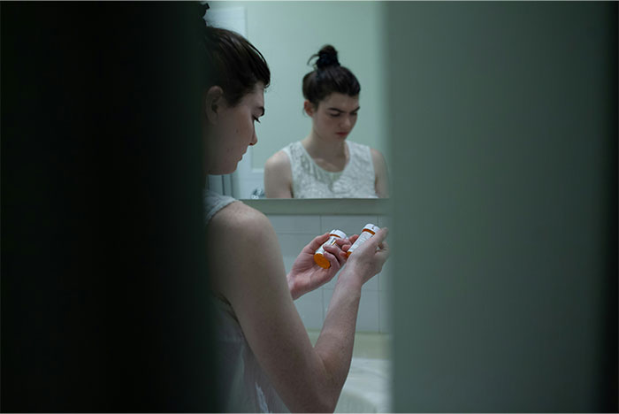 A young woman looking at medication bottles in a bathroom, reflecting on ways people got permanently banned from a friend’s house.
