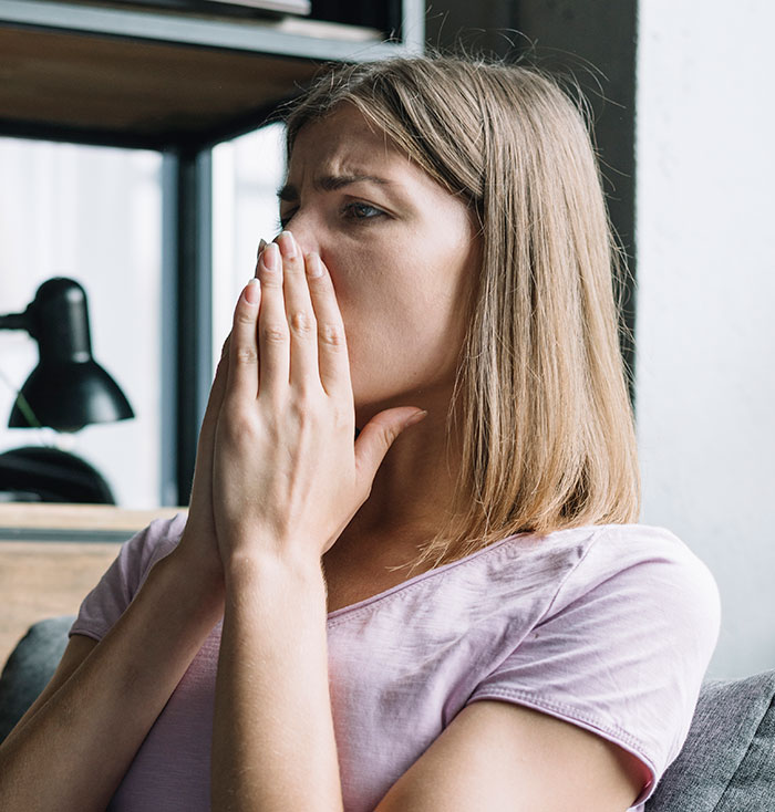 Woman in a pink shirt looking worried, covering her mouth with hands, depicting stress after messing up at work.