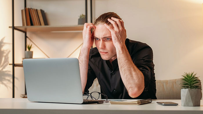 Young man stressed at his laptop, showing frustration and regret while working, illustrating people badly messed up at work.