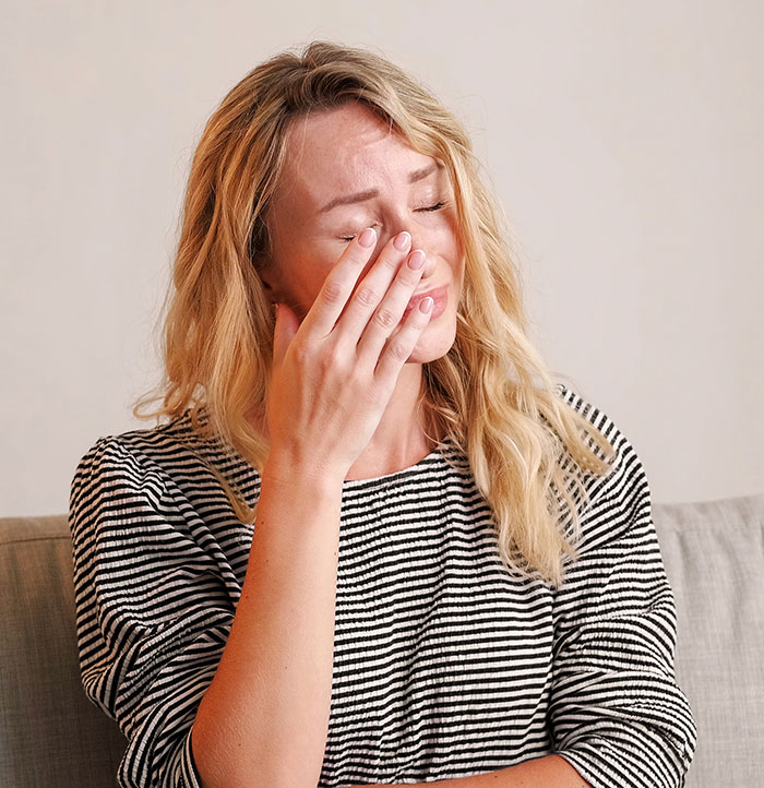 Woman in striped shirt wiping tears from eye, reflecting on moments people badly messed up at work and survived.