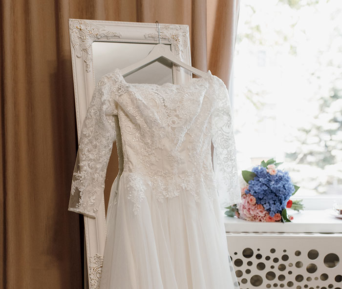 White lace wedding dress hanging on a decorative frame near a window with a bouquet, representing work mishaps and recovery.