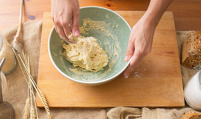 Hands mixing dough in a bowl on a wooden board, illustrating a work fail moment from people who messed up at work.