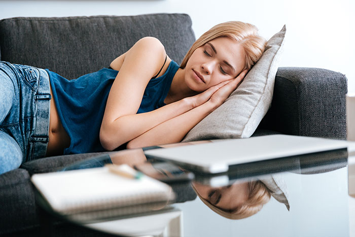 Young woman resting on a couch with eyes closed, surrounded by work items, depicting people who messed up at work.