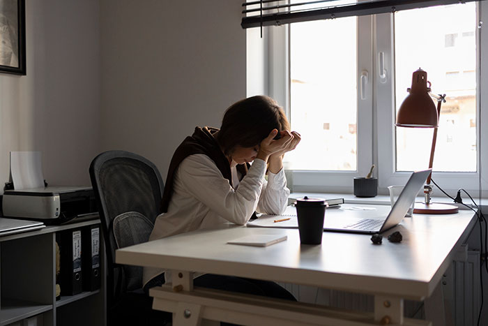 Woman sitting at desk with head in hands, showing frustration and stress from work mistakes in home office setting.