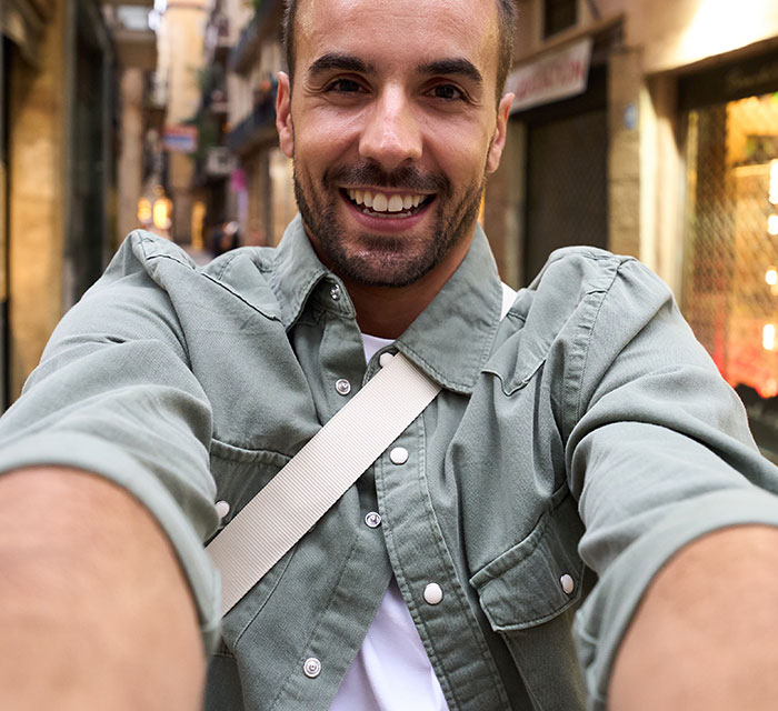 Smiling man taking a selfie on a busy street, illustrating moments people badly messed up at work and lived.