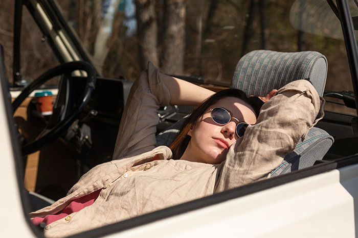 Young woman wearing sunglasses resting inside a car, illustrating a moment after a work mishap in a relatable setting.