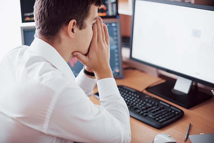 Man in white shirt stressed at work desk with computer, representing people badly messed up at work and coping.