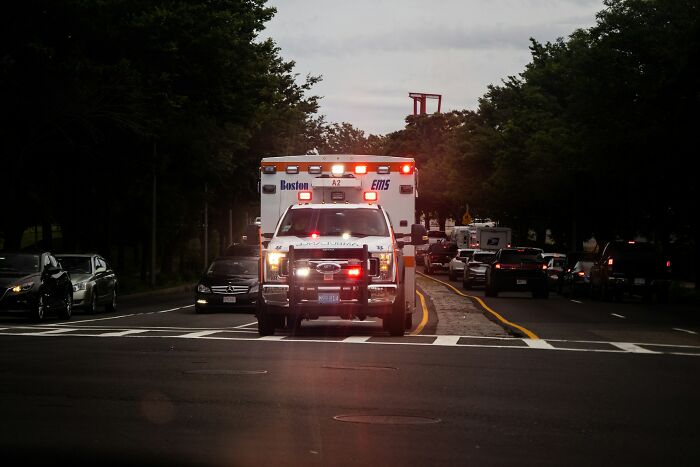 Ambulance with flashing lights on a city street, responding to an emergency related to unusual ways people died.