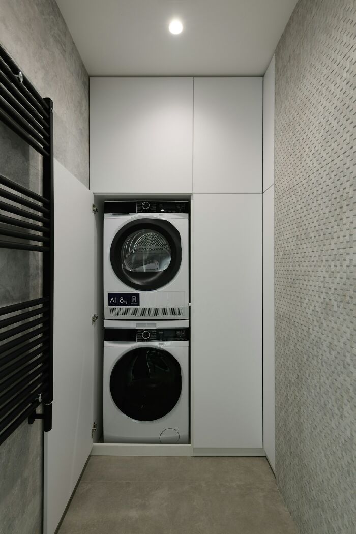 Modern laundry room with stacked washer and dryer inside white cabinetry, highlighting convenience and storage solutions.