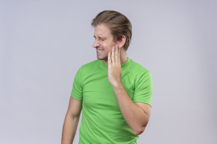 Young man in green shirt touching his face in pain, representing a patient with a rare disease experience