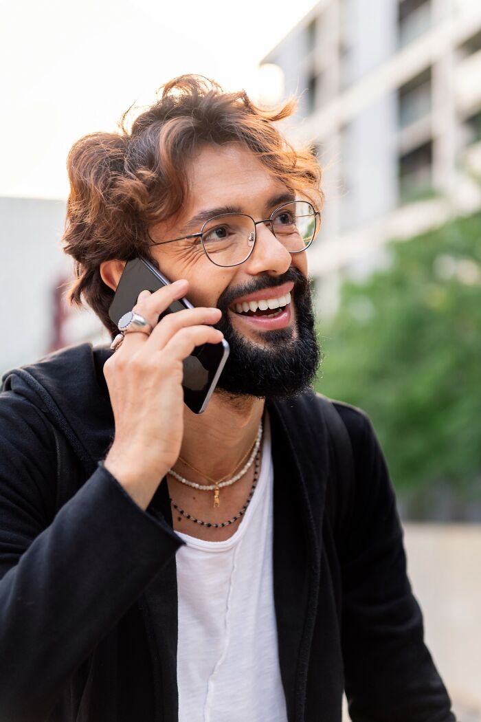 Man with glasses smiling and talking on phone outdoors, representing Americans finding a loophole to use it.