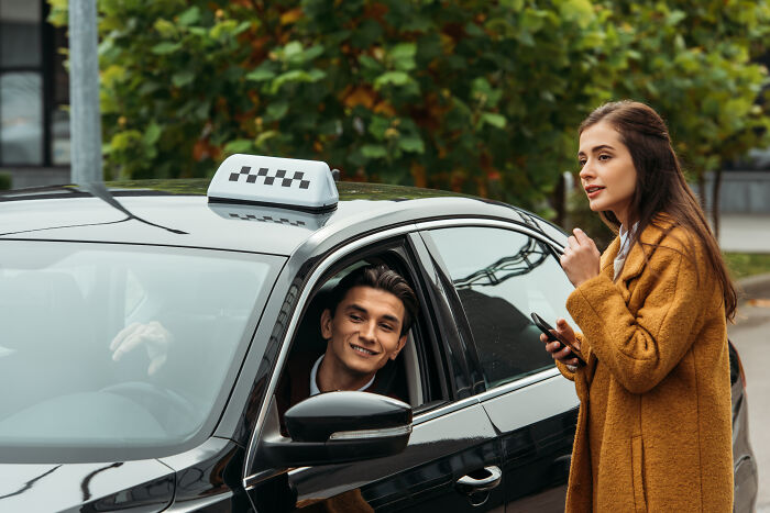 Young woman sharing things with a taxi driver during a conversation outside the car in an urban setting