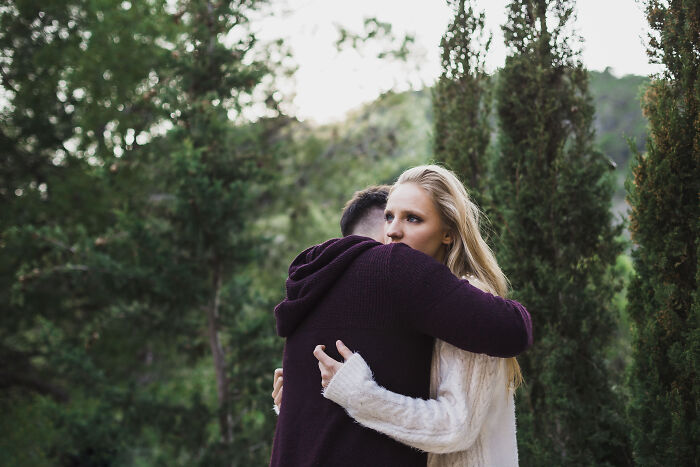 A young woman and man hugging outdoors in a forest setting, sharing emotions they would never admit in real life.