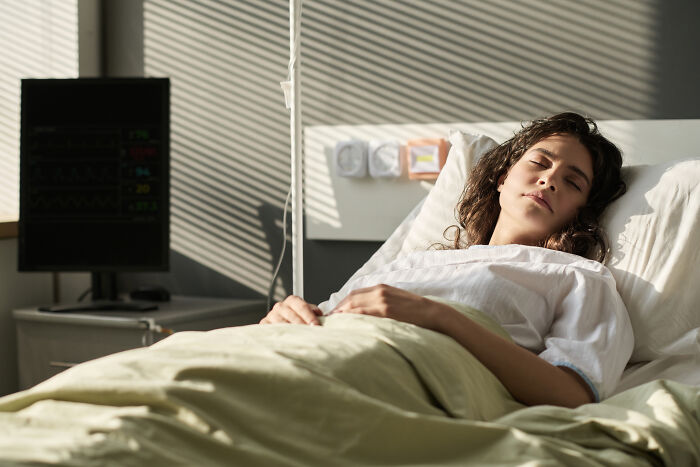 Young woman resting in hospital bed with medical monitor nearby, reflecting doctors and nurses experiences in healthcare settings.