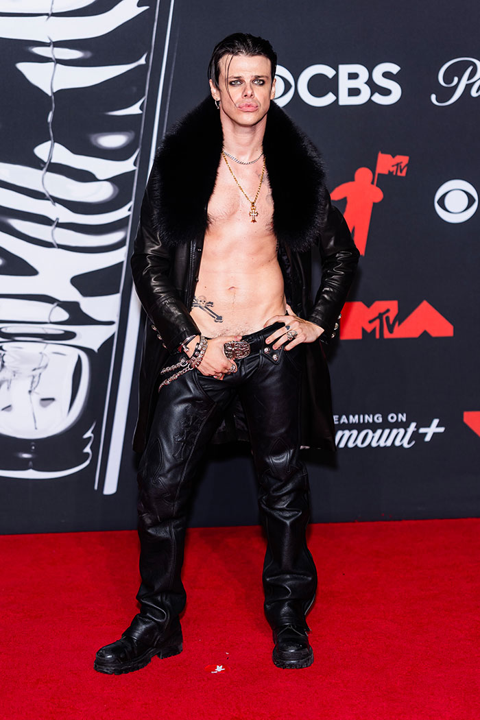 Shirtless man in black fur-collared coat and leather pants posing on red carpet at 2025 Video Music Awards worst dressed stars.