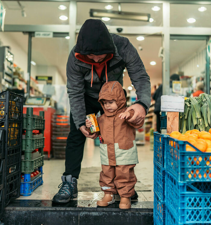 Parent helping toddler in raincoat at grocery store, illustrating parenting hacks that save sanity during outings.