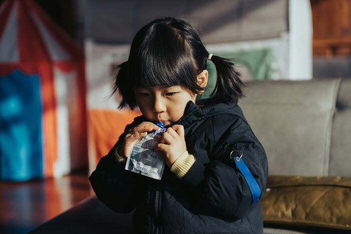 Young child drinking from a pouch indoors, illustrating practical parenting hacks to save sanity in everyday life.