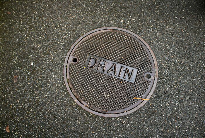 Close-up of a metal drain cover on asphalt, representing people who work and explore beneath our feet.
