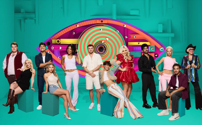 Big Brother housemates posing in colorful outfits with a large eye logo in the background during the latest season.