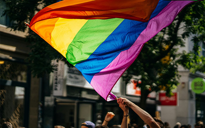 Rainbow pride flag waved by raised hands outdoors, symbolizing LGBTQ+ community in a men-only gay bar controversy.