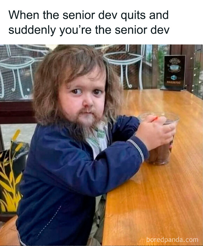 Child with a beard sitting at a wooden table holding a drink, illustrating programming and computer science meme humor.