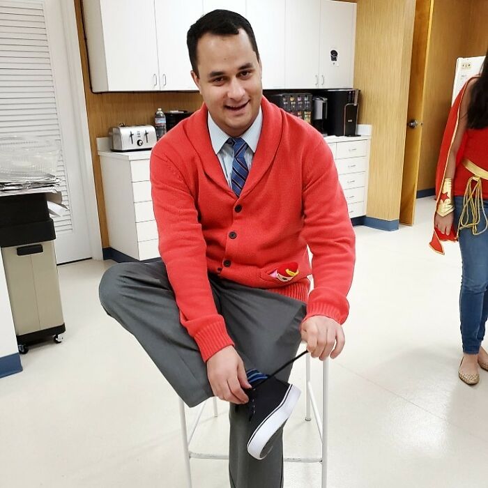 Man spending years transforming into the many faces of Tom Hanks, dressed in a red cardigan and gray pants, indoors.