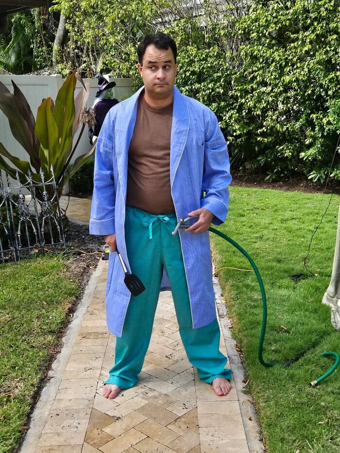 Man transforming into the many faces of Tom Hanks, dressed in casual clothes and holding a spatula and garden hose.