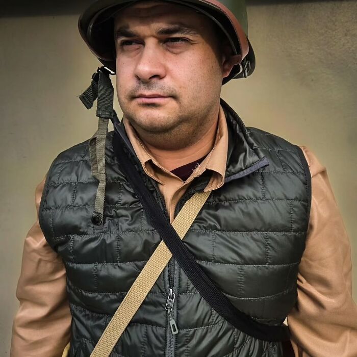 Man dressed as Tom Hanks character, wearing military-style helmet and vest, showcasing transformation into Tom Hanks faces.