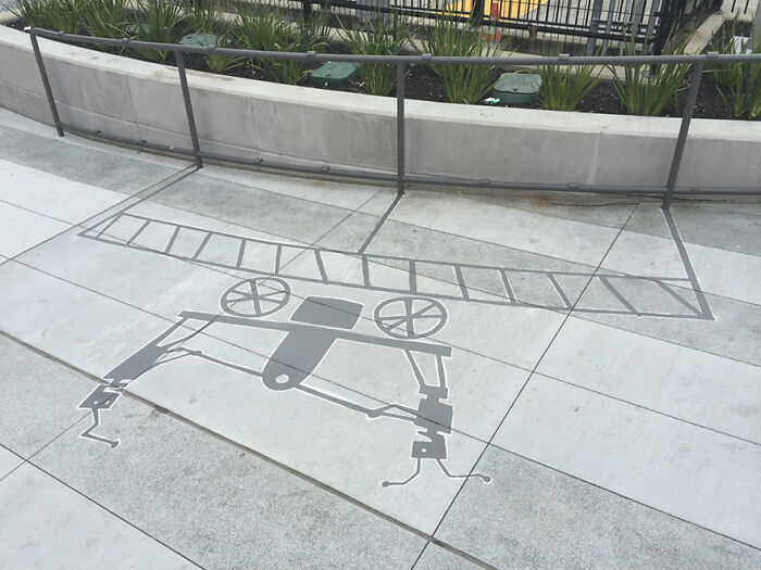 Shadow art installation on sidewalk creating an illusion of a vintage car on train tracks in an urban setting.